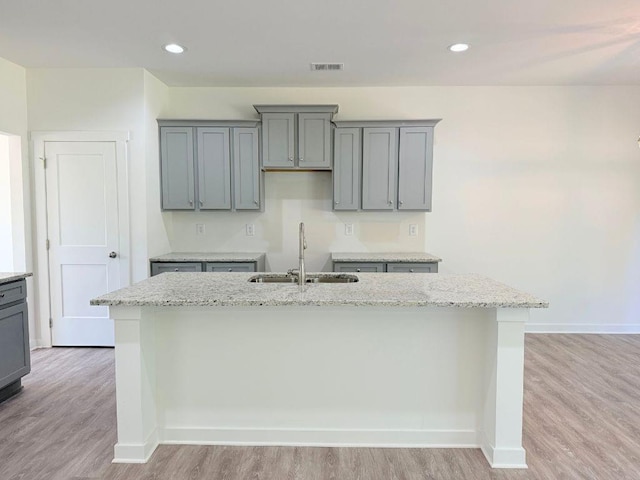 kitchen featuring a sink, a kitchen island with sink, light wood-type flooring, gray cabinetry, and visible vents
