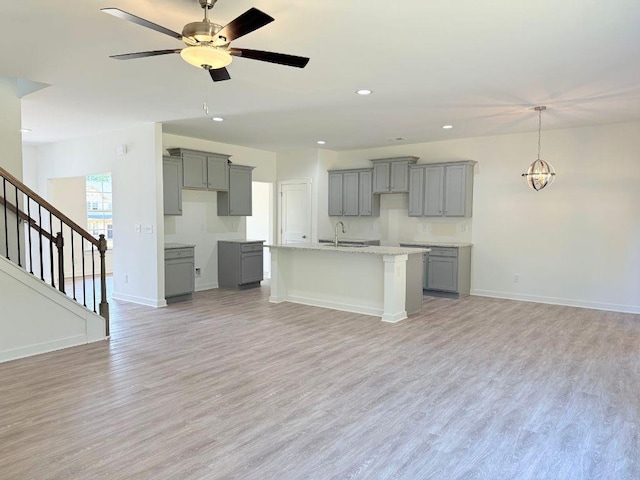 kitchen with a kitchen island with sink, light wood-style flooring, a sink, baseboards, and gray cabinetry