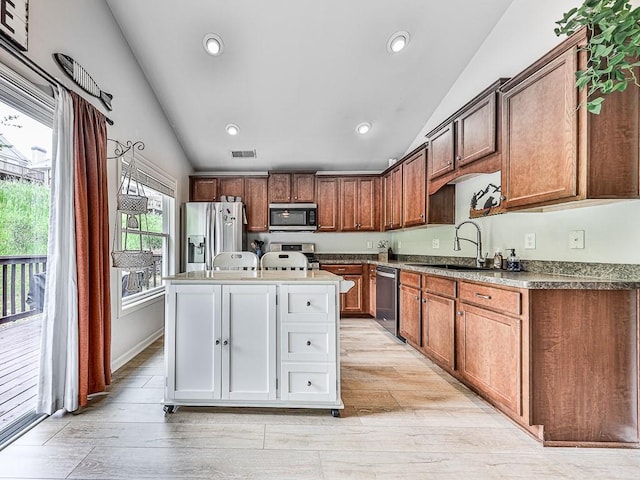 kitchen with lofted ceiling, sink, light hardwood / wood-style flooring, appliances with stainless steel finishes, and an island with sink