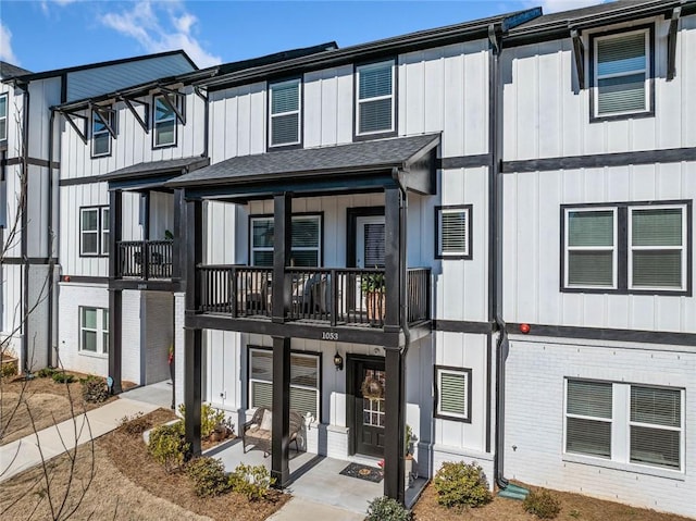 multi unit property featuring a balcony, a shingled roof, board and batten siding, and brick siding