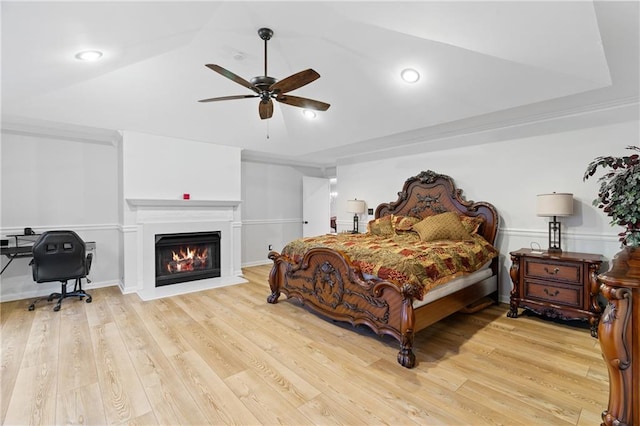 bedroom with a ceiling fan, a glass covered fireplace, wood finished floors, and lofted ceiling