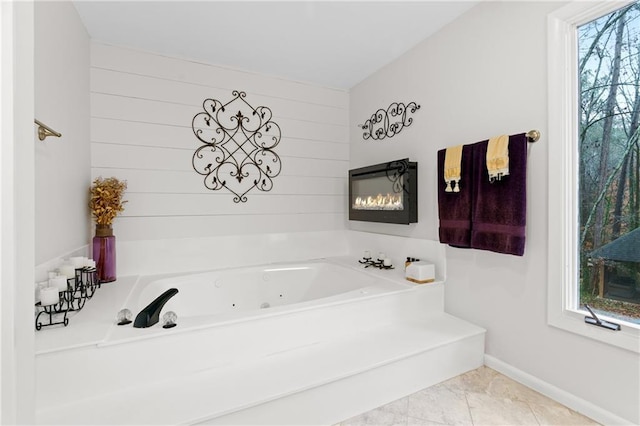 full bathroom featuring a jetted tub, baseboards, a glass covered fireplace, and wood walls