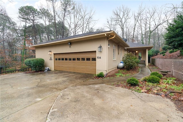 view of property exterior with fence, an attached garage, and driveway