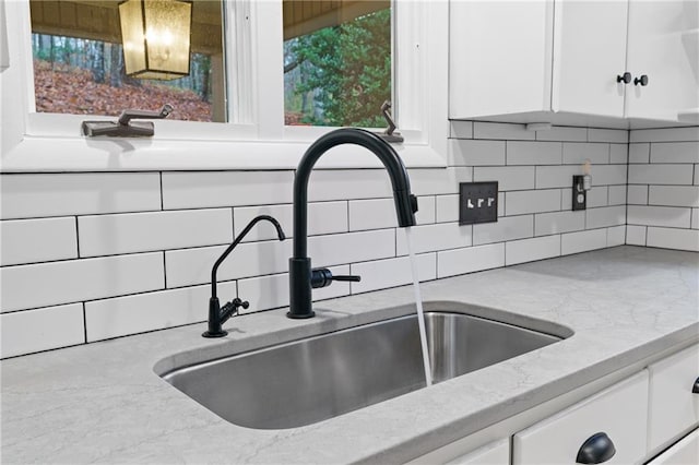 room details featuring a sink, light stone countertops, backsplash, and white cabinetry