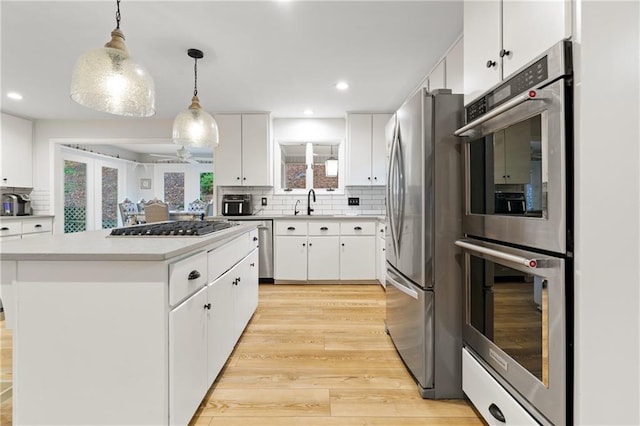 kitchen with appliances with stainless steel finishes, a center island, decorative light fixtures, decorative backsplash, and light wood-type flooring