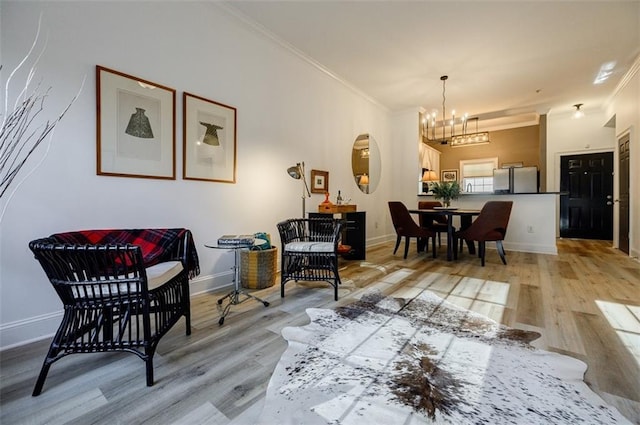 sitting room with ornamental molding, an inviting chandelier, and light wood-type flooring