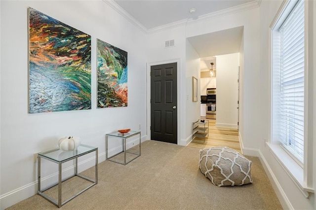 sitting room with ornamental molding, plenty of natural light, and light colored carpet