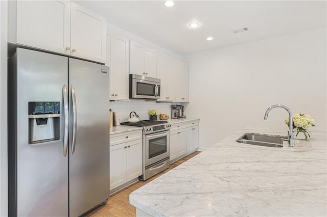 kitchen featuring visible vents, a sink, appliances with stainless steel finishes, light wood finished floors, and decorative backsplash