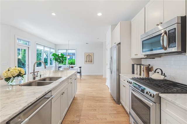 kitchen featuring light stone countertops, decorative backsplash, light wood-style flooring, stainless steel appliances, and a sink