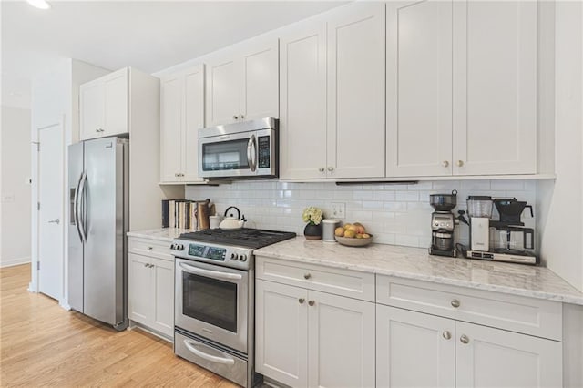 kitchen featuring light stone counters, tasteful backsplash, appliances with stainless steel finishes, and light wood-style flooring