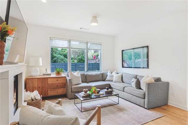 living area with visible vents, baseboards, a warm lit fireplace, and wood finished floors