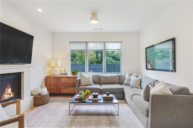 living area with visible vents, recessed lighting, a glass covered fireplace, and wood finished floors