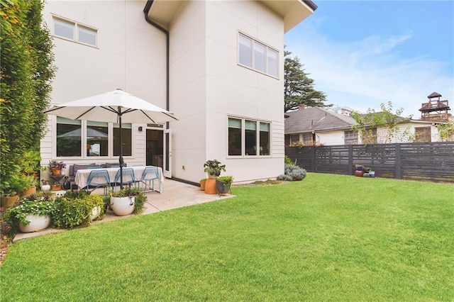 rear view of property with a yard, a patio area, stucco siding, and fence