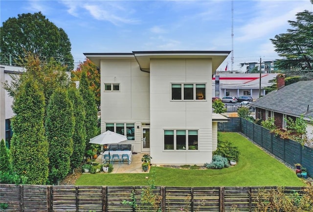 rear view of house with a yard, stucco siding, a patio, and a fenced backyard