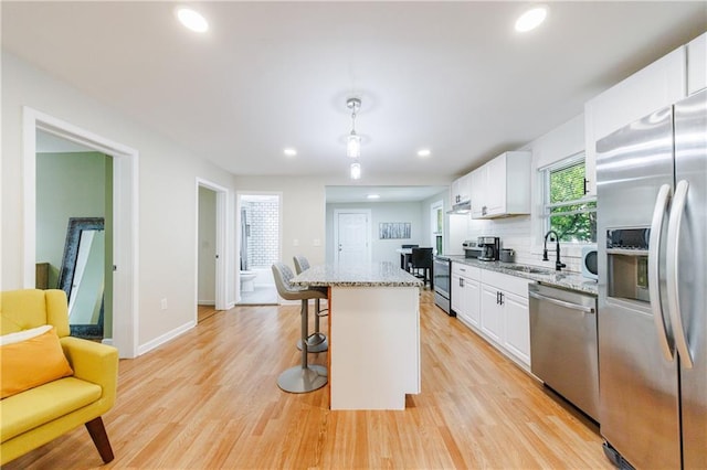 kitchen with light stone counters, stainless steel appliances, sink, white cabinets, and a center island