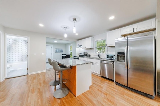 kitchen with light stone countertops, stainless steel appliances, a kitchen island, pendant lighting, and white cabinetry