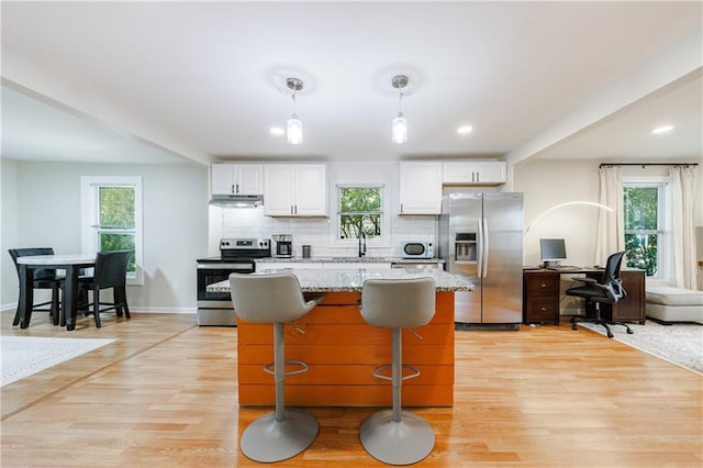 kitchen with pendant lighting, white cabinets, light stone countertops, a wealth of natural light, and appliances with stainless steel finishes