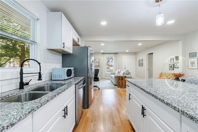 kitchen featuring decorative backsplash, stainless steel dishwasher, sink, white cabinets, and light hardwood / wood-style floors