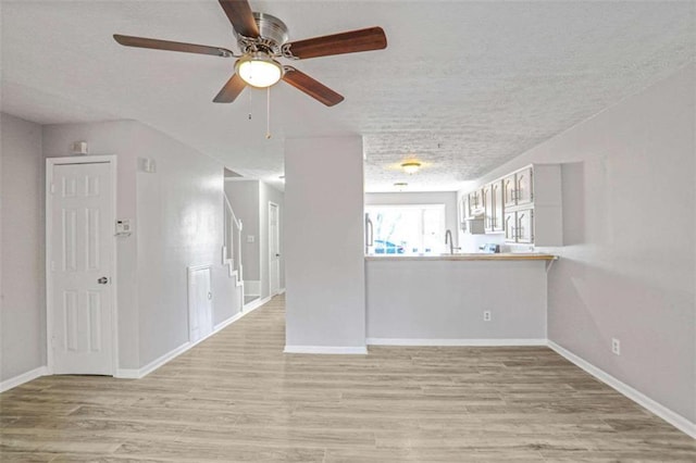 spare room featuring a sink, baseboards, light wood finished floors, and a textured ceiling