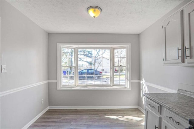 dining space featuring light wood finished floors, a textured ceiling, and baseboards