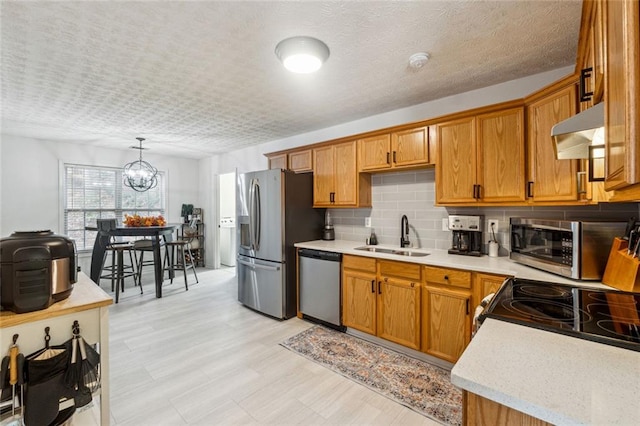 kitchen featuring sink, a notable chandelier, pendant lighting, exhaust hood, and appliances with stainless steel finishes