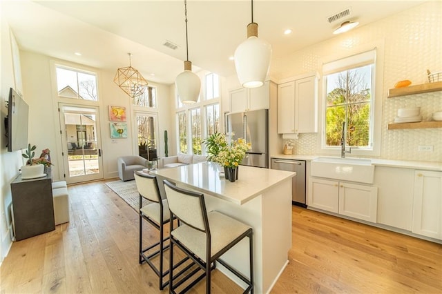 kitchen featuring a sink, white cabinetry, light countertops, appliances with stainless steel finishes, and decorative light fixtures