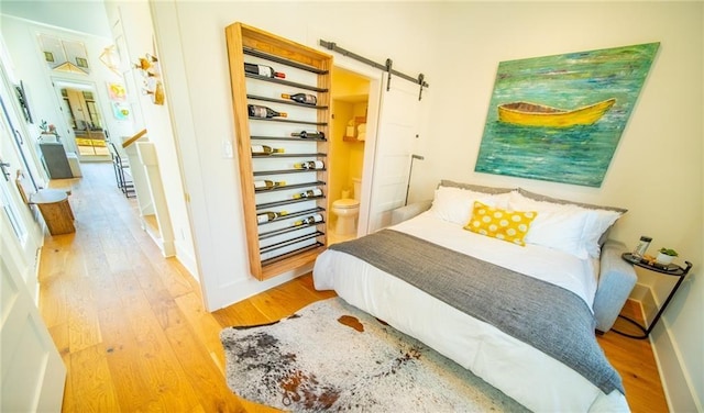 bedroom with baseboards, light wood finished floors, and a barn door