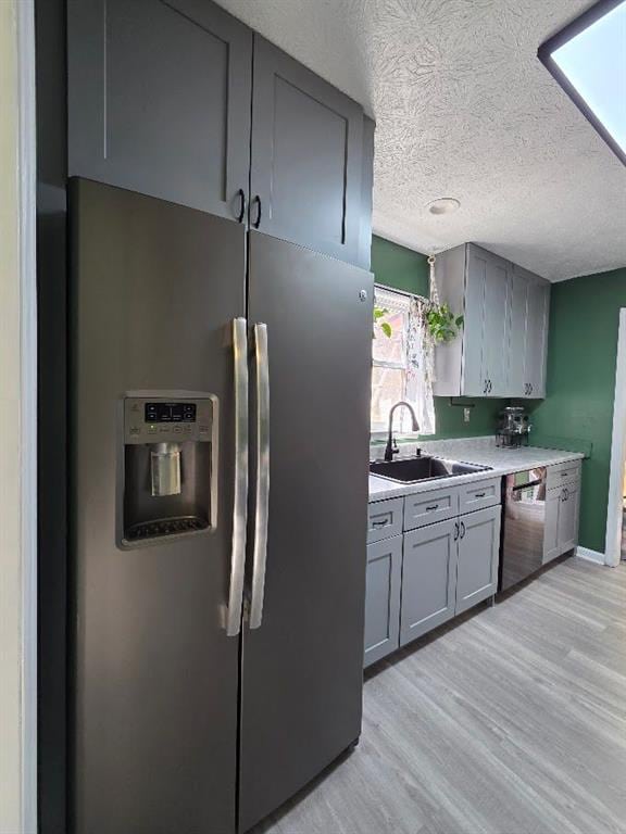 kitchen with light wood-style flooring, stainless steel appliances, a sink, light countertops, and gray cabinets