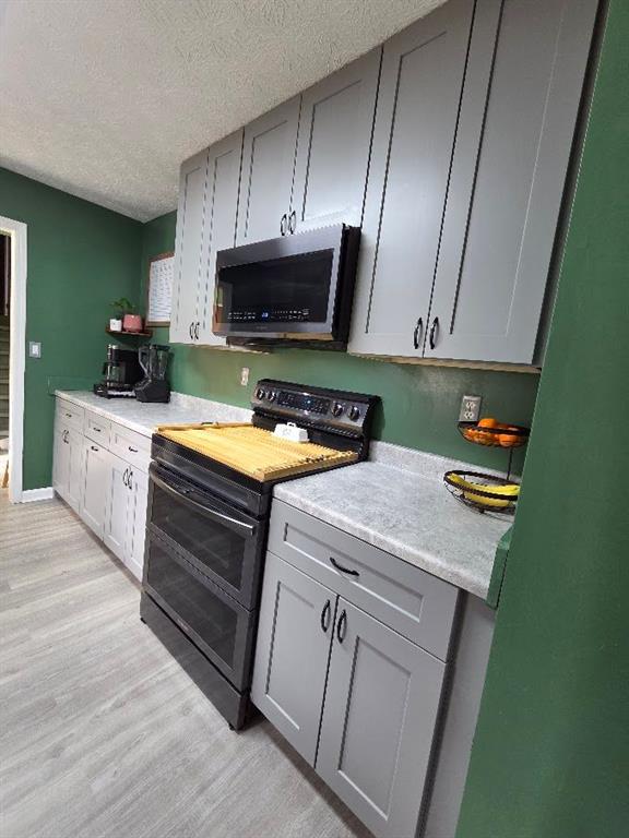 kitchen featuring range with two ovens, gray cabinets, light countertops, stainless steel microwave, and a textured ceiling