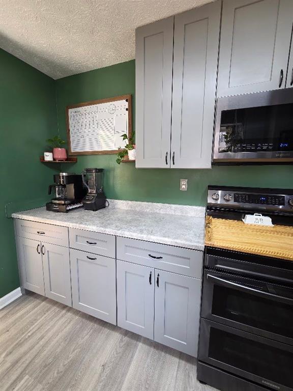 kitchen featuring a textured ceiling, light countertops, gray cabinets, light wood finished floors, and stainless steel microwave