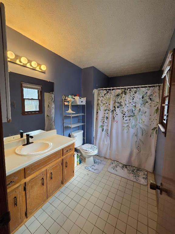 full bathroom featuring a shower with shower curtain, toilet, tile patterned floors, a textured ceiling, and vanity