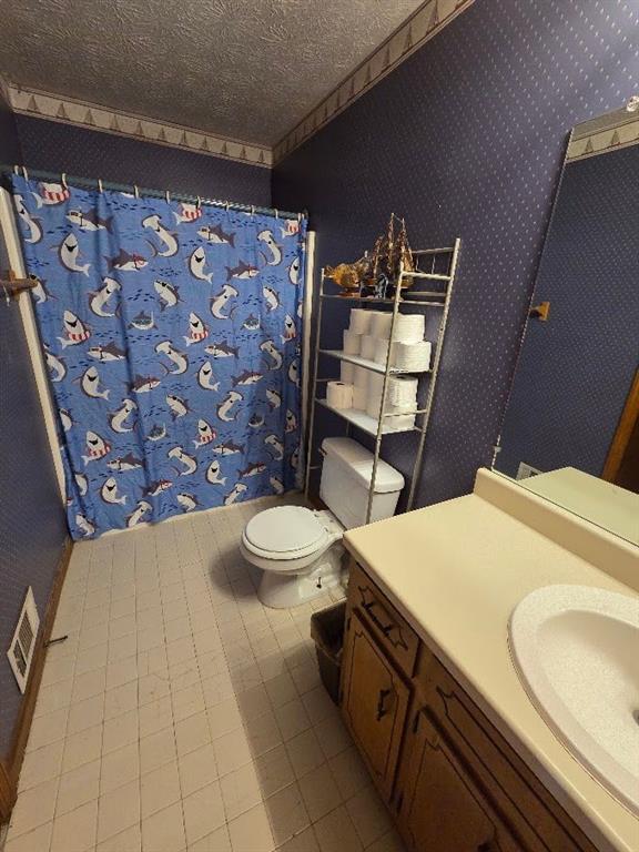 full bath with visible vents, toilet, vanity, a textured ceiling, and wallpapered walls