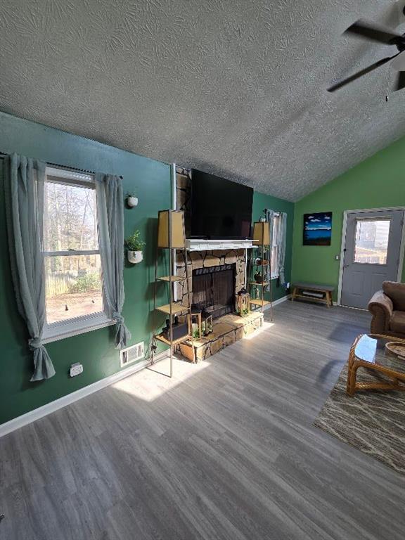 living area with lofted ceiling, visible vents, a fireplace, and wood finished floors