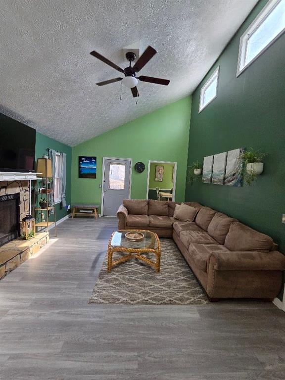 living area featuring lofted ceiling, a textured ceiling, a fireplace, wood finished floors, and a ceiling fan