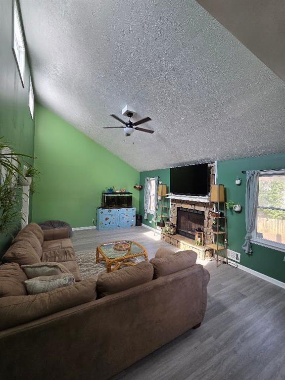 living room with lofted ceiling, a stone fireplace, a textured ceiling, wood finished floors, and baseboards