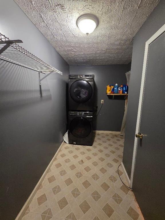 washroom featuring laundry area, stacked washer and clothes dryer, a textured ceiling, and baseboards