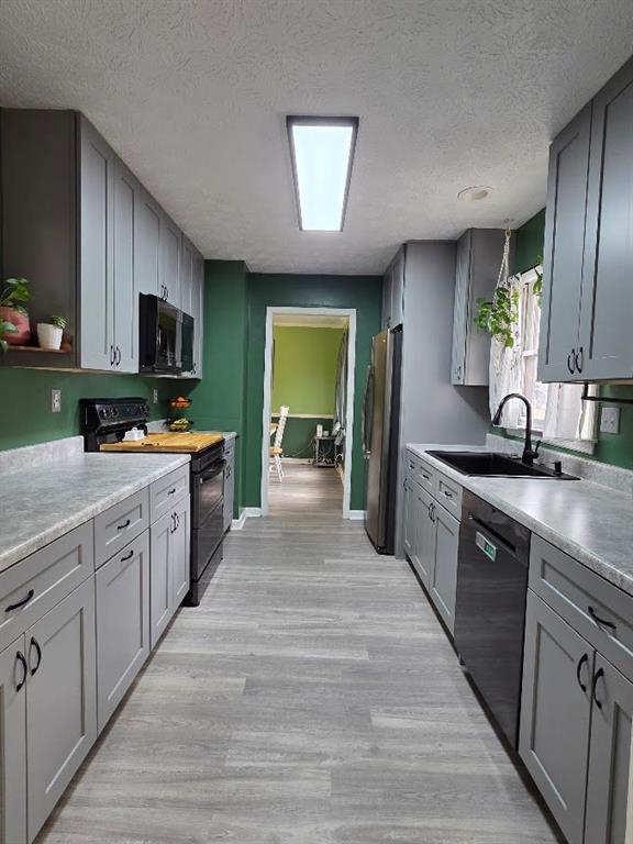 kitchen featuring light wood finished floors, a textured ceiling, gray cabinetry, black appliances, and a sink