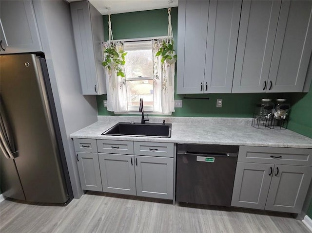 kitchen featuring a sink, light countertops, gray cabinets, freestanding refrigerator, and dishwasher