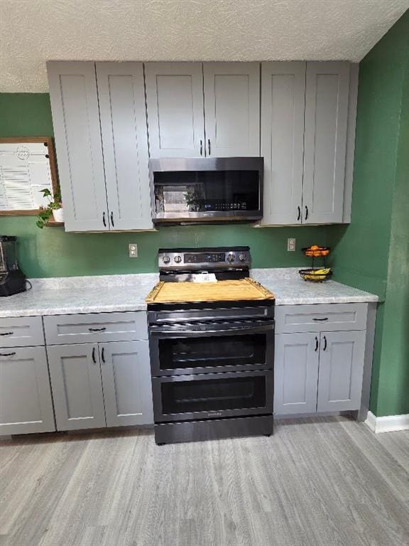 kitchen featuring a textured ceiling, gray cabinetry, stainless steel appliances, light countertops, and light wood-type flooring