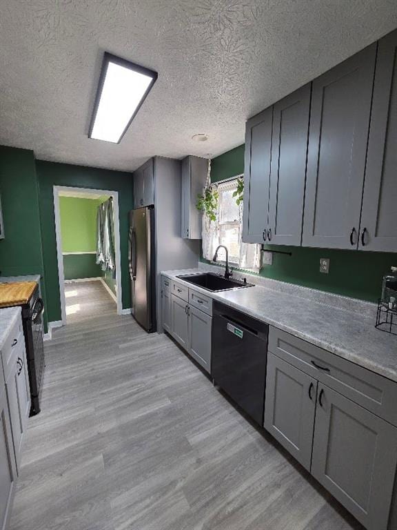 kitchen featuring light wood finished floors, gray cabinetry, freestanding refrigerator, a sink, and dishwasher