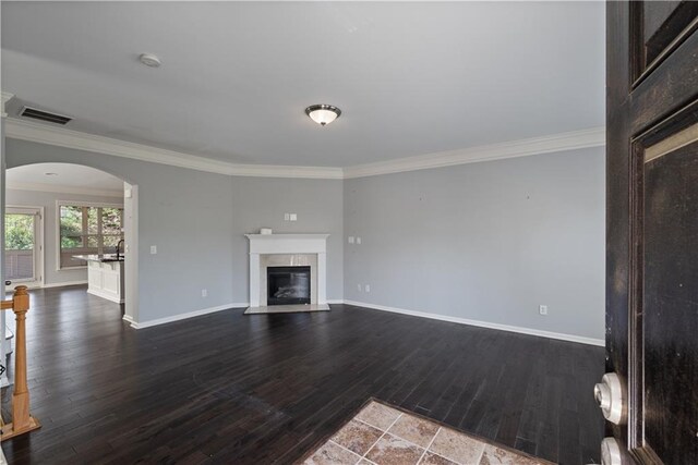 unfurnished living room featuring arched walkways, ornamental molding, dark wood-type flooring, a fireplace with flush hearth, and baseboards