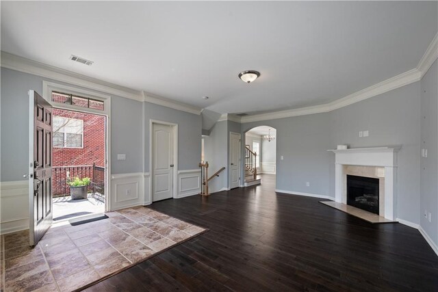unfurnished living room with wood finished floors, arched walkways, ornamental molding, plenty of natural light, and wainscoting