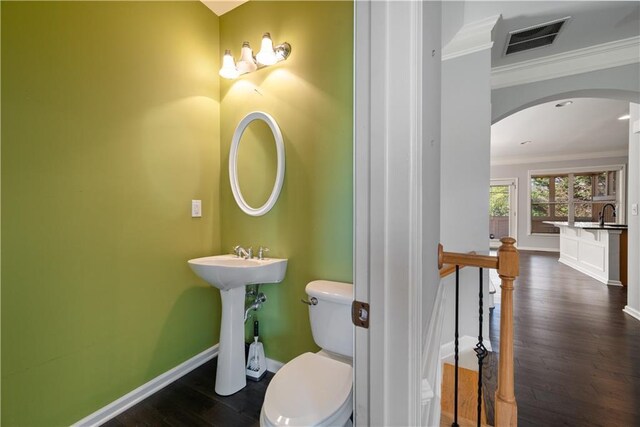half bathroom with ornamental molding, toilet, wood finished floors, and baseboards
