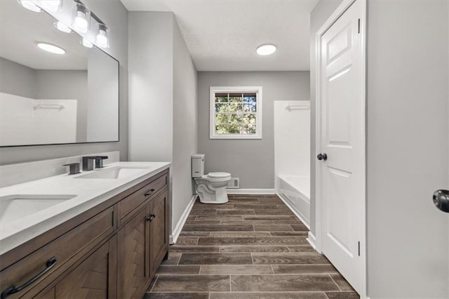 full bath featuring wood finish floors, toilet, a sink, double vanity, and baseboards