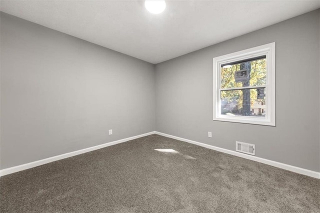 spare room with dark carpet, visible vents, and baseboards