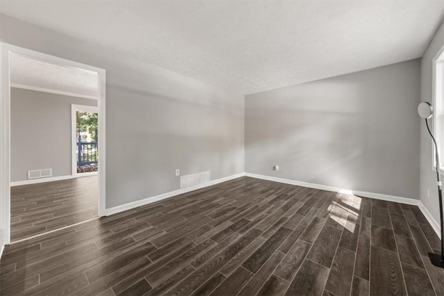 spare room featuring a textured ceiling, baseboards, dark wood-style floors, and visible vents