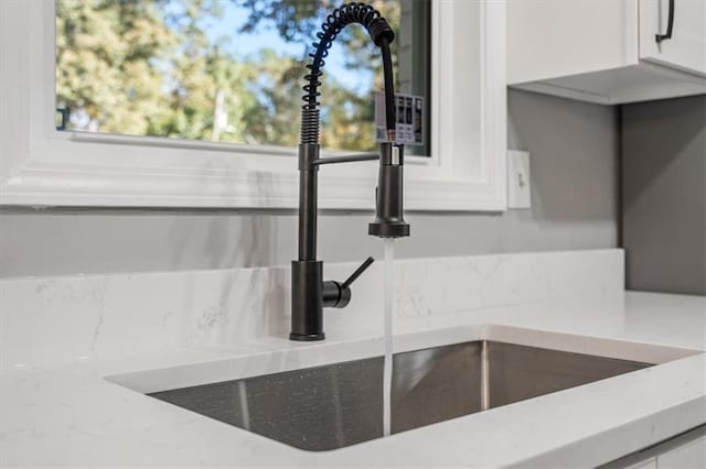 interior details with light stone countertops, decorative backsplash, a sink, and white cabinets