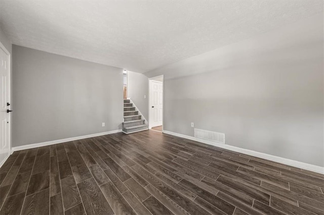 unfurnished living room featuring visible vents, baseboards, a textured ceiling, stairs, and dark wood-type flooring