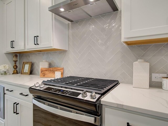 kitchen with light stone countertops, stainless steel range with gas cooktop, white cabinets, and ventilation hood