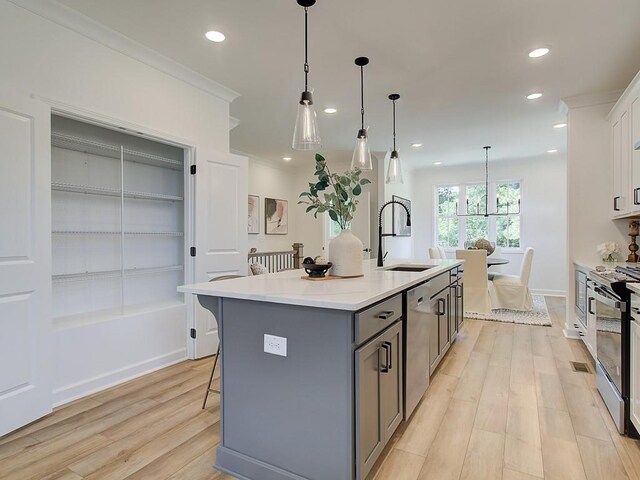 kitchen with appliances with stainless steel finishes, sink, white cabinetry, gray cabinetry, and a center island with sink